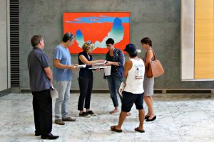 Woman with clipboard standing with five people in art gallery