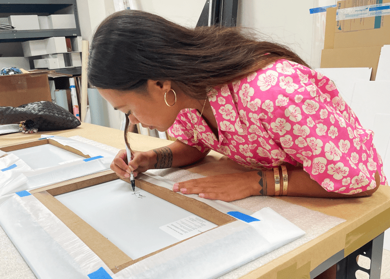 Haʻa Keaulana signing the back of a photograph.