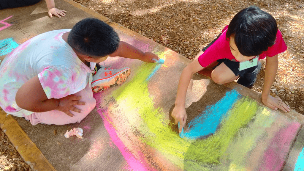 Students drawing with chalk on a school sidewalk.