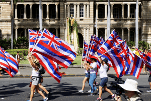 Celebration parade participants holding Hawaiian flags.