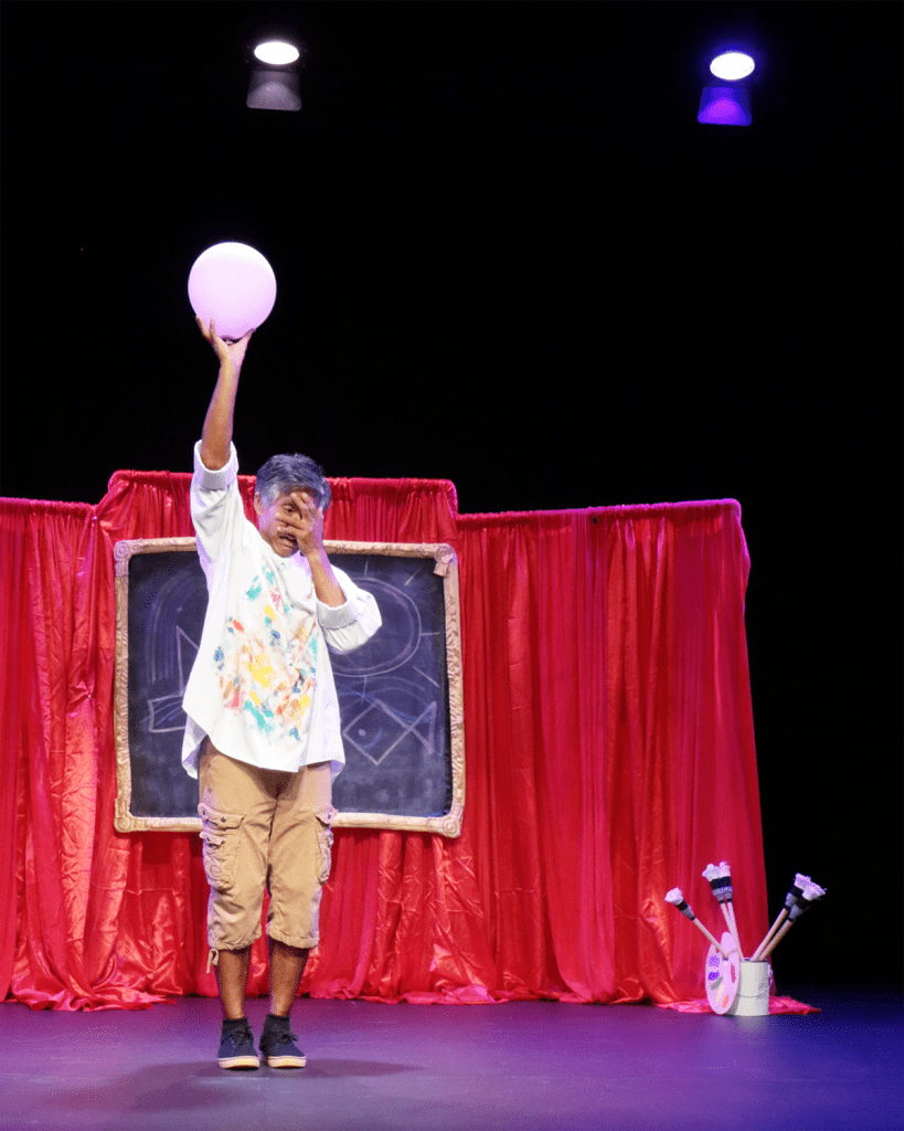 Performer pretending that a balloon is beginning to lift them off the ground. Performer's expression suggests fear.