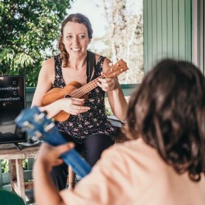 Teacher Melissa Sigh holding a ukulele. Melissa is seated and facing a student.