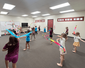 Students and teacher in a classroom. Each person holds a ribbon streamer in multiple colors.