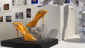Photo of museum gallery. Sculpture shaped like a pair of high heeled shoes, made out of pencils. Sculpture is "Heels of Power" by Dylan Cohen, student at ʻIolani School.