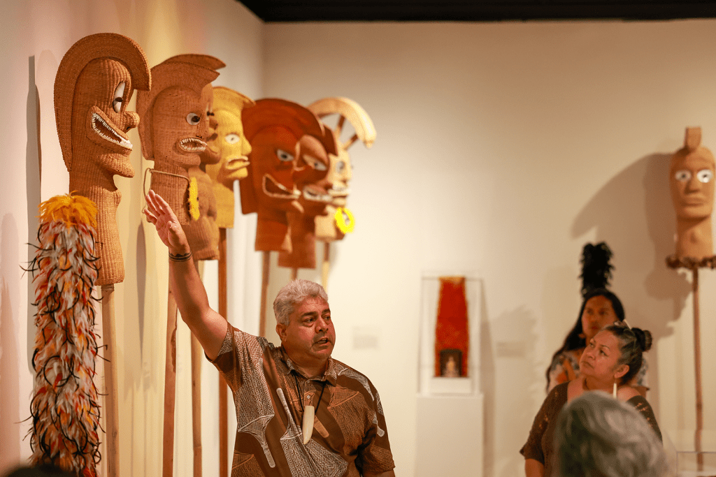 Lloyd and Haunani Sing in a Hawaii State Art Museum gallery. Lloyd is leading a tour of an exhibit featuring twined basketry sculptures made by their students.