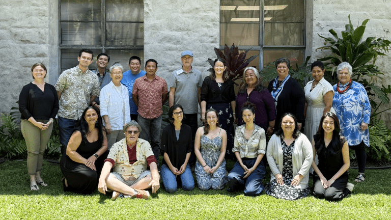 Group of people standing, kneeling, and sitting on a lawn in front of a building.